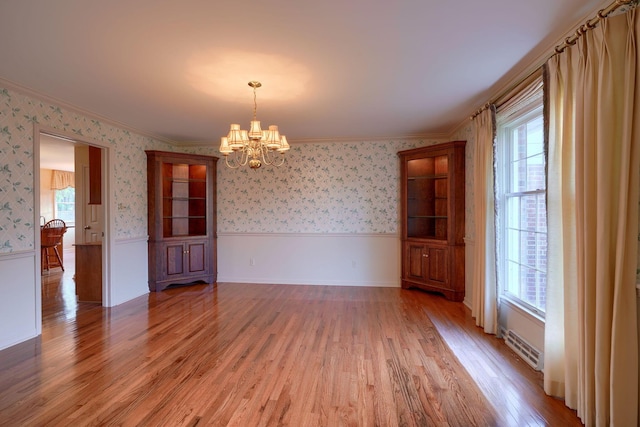 spare room featuring hardwood / wood-style flooring, plenty of natural light, crown molding, and a notable chandelier