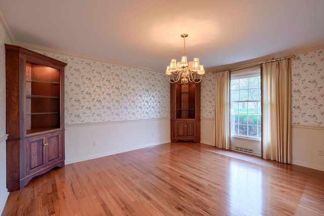 empty room featuring light hardwood / wood-style floors, crown molding, and a notable chandelier