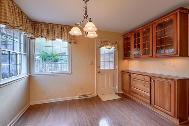 unfurnished dining area featuring light hardwood / wood-style flooring, a healthy amount of sunlight, and a notable chandelier