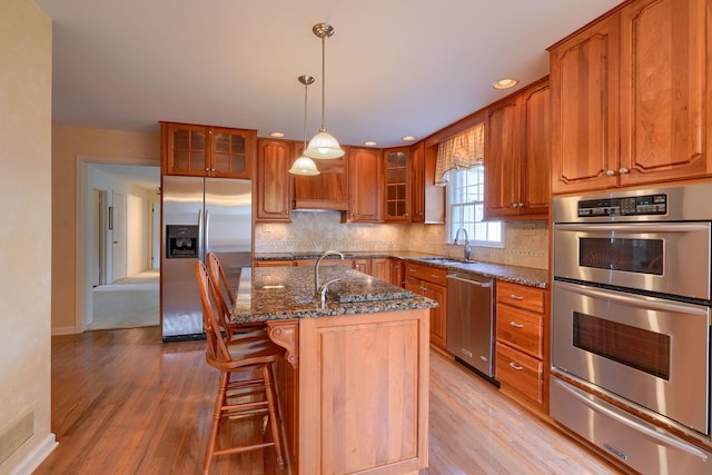 kitchen with dark stone countertops, a center island with sink, stainless steel appliances, and light hardwood / wood-style floors