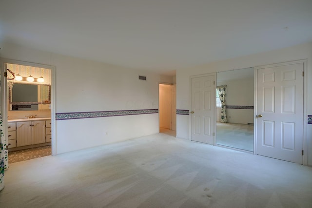 unfurnished bedroom featuring a closet, sink, light carpet, and ensuite bath