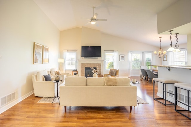 living room with hardwood / wood-style flooring, ceiling fan with notable chandelier, a tile fireplace, and high vaulted ceiling