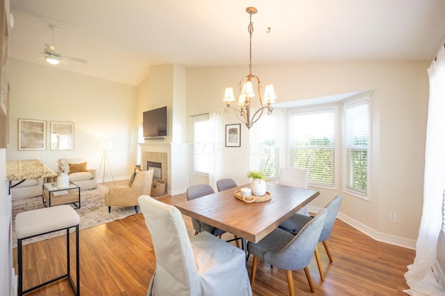 dining room featuring a tile fireplace, ceiling fan with notable chandelier, hardwood / wood-style flooring, and lofted ceiling