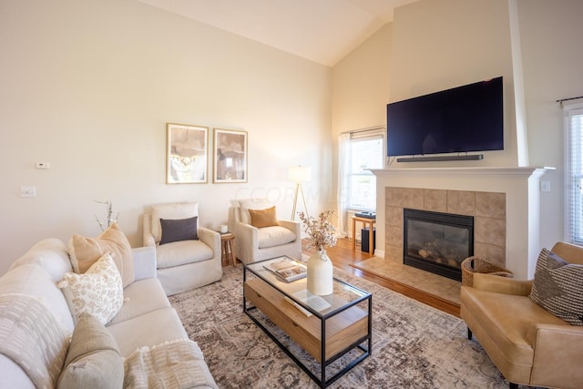 living room featuring a tile fireplace, hardwood / wood-style floors, and high vaulted ceiling