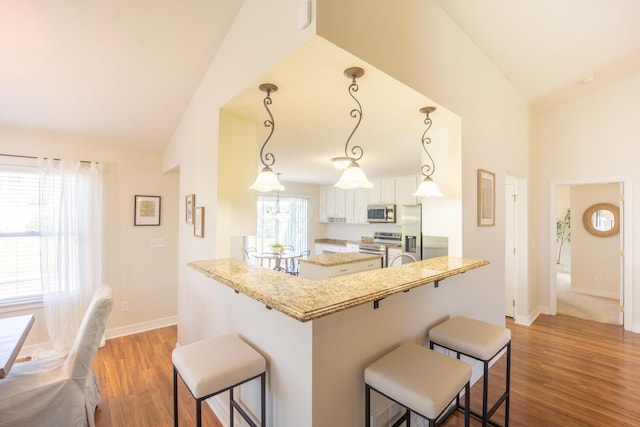 kitchen featuring a breakfast bar area, kitchen peninsula, hanging light fixtures, and vaulted ceiling