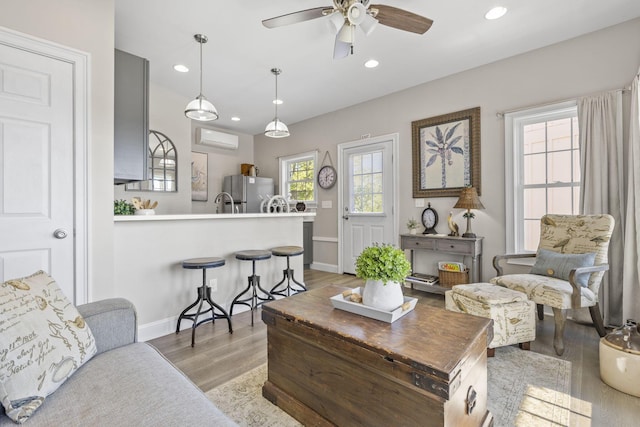 living room with a wall mounted air conditioner, light wood-type flooring, and ceiling fan