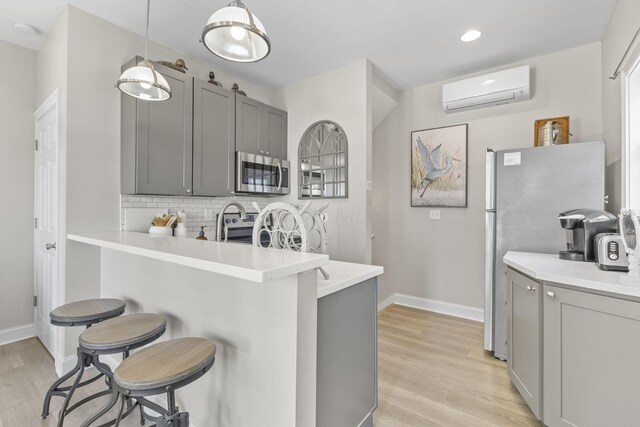 kitchen featuring a wall mounted AC, kitchen peninsula, a breakfast bar area, gray cabinets, and appliances with stainless steel finishes