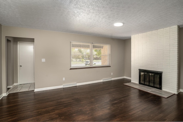 unfurnished living room with baseboard heating, wood-type flooring, a textured ceiling, and a brick fireplace