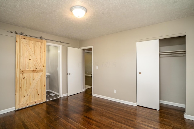 unfurnished bedroom with a barn door, dark hardwood / wood-style flooring, ensuite bathroom, a textured ceiling, and a closet