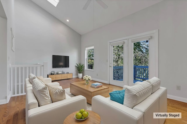 living room featuring ceiling fan, a skylight, high vaulted ceiling, and light hardwood / wood-style flooring