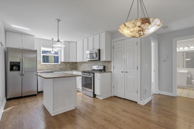 kitchen with light wood-type flooring, stainless steel appliances, white cabinets, a kitchen island, and hanging light fixtures