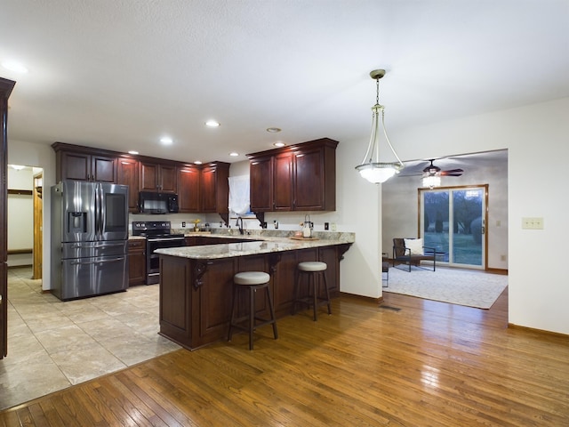 kitchen with a breakfast bar area, hanging light fixtures, light wood-type flooring, kitchen peninsula, and stainless steel appliances