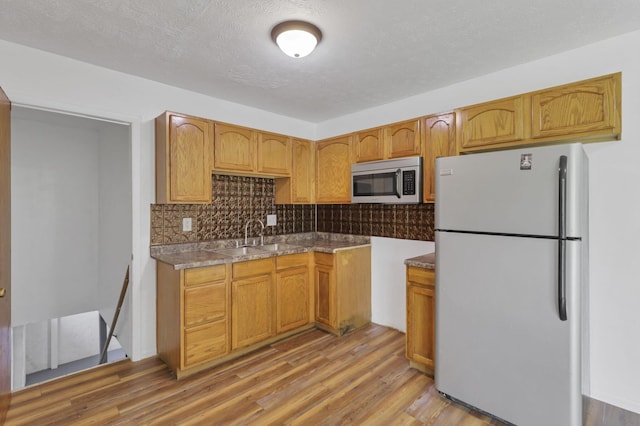 kitchen with white refrigerator, sink, decorative backsplash, light wood-type flooring, and a textured ceiling