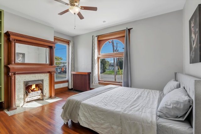 bedroom featuring radiator, ceiling fan, a fireplace, and light hardwood / wood-style floors