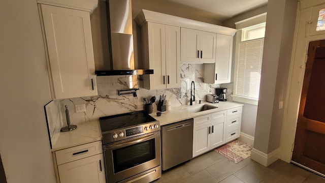 kitchen with backsplash, stainless steel appliances, sink, wall chimney range hood, and white cabinetry