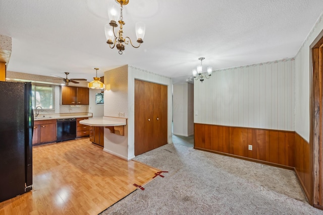 kitchen featuring light hardwood / wood-style flooring, wood walls, pendant lighting, black appliances, and ceiling fan with notable chandelier