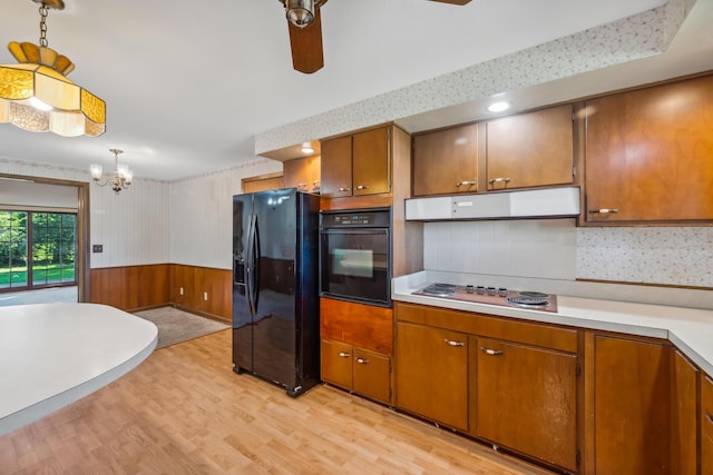 kitchen with range hood, wood walls, pendant lighting, light hardwood / wood-style floors, and black appliances