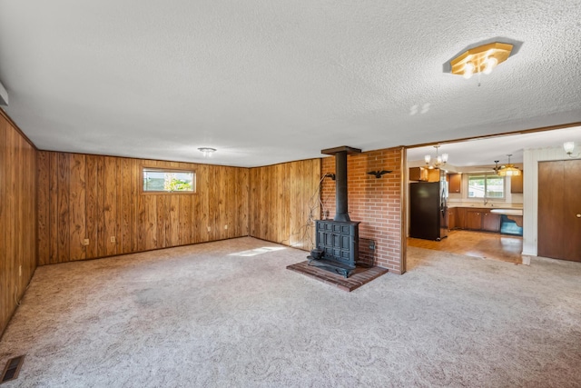 unfurnished living room with a wood stove, a wealth of natural light, light carpet, and wood walls