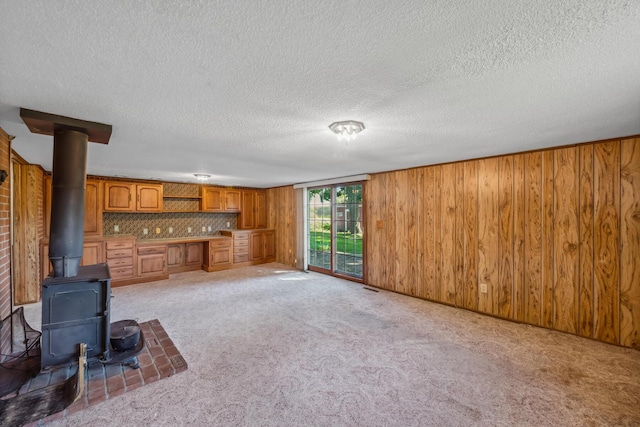 unfurnished living room with carpet flooring, a wood stove, wooden walls, and a textured ceiling