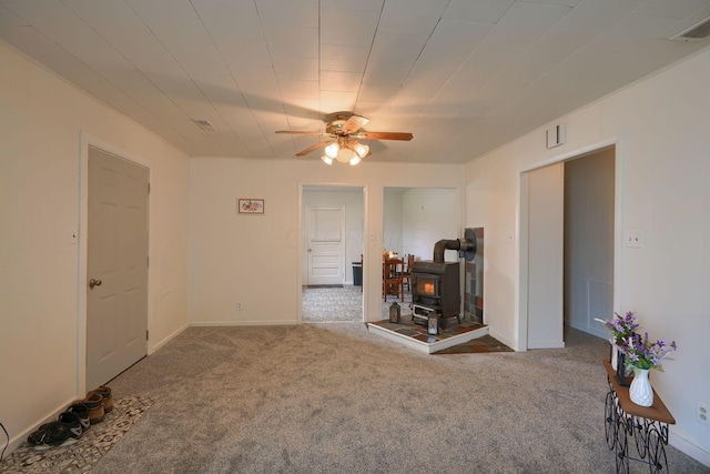 empty room with ceiling fan, a wood stove, and carpet floors