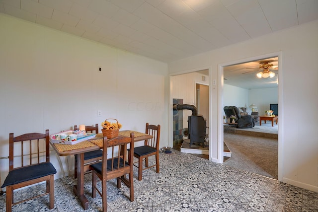 carpeted dining room featuring a wood stove and ceiling fan