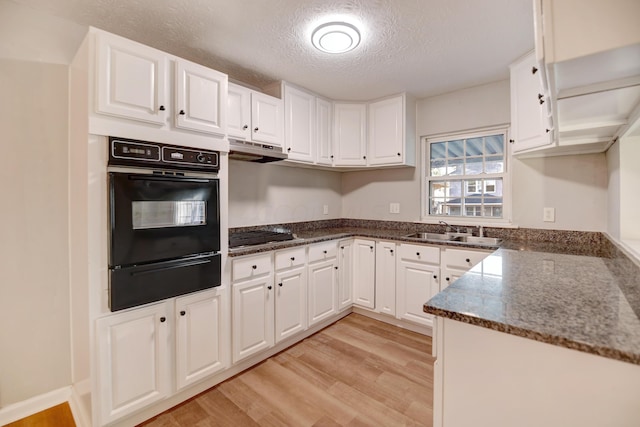 kitchen with sink, light hardwood / wood-style floors, a textured ceiling, black oven, and white cabinets