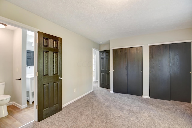 unfurnished bedroom featuring multiple closets, ensuite bathroom, light colored carpet, and a textured ceiling