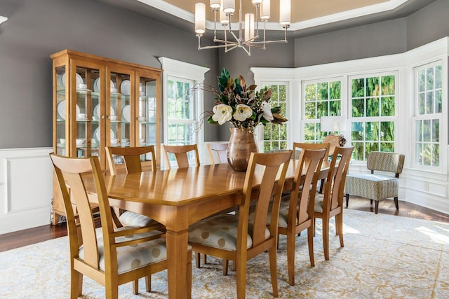 dining space with wood-type flooring, an inviting chandelier, a raised ceiling, and crown molding