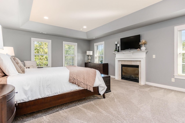 bedroom featuring a fireplace, light colored carpet, a raised ceiling, and multiple windows