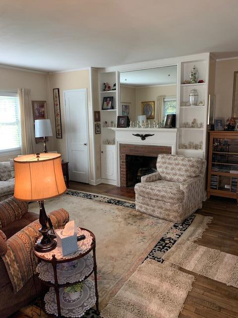 living room with built in shelves, dark hardwood / wood-style flooring, a brick fireplace, and crown molding