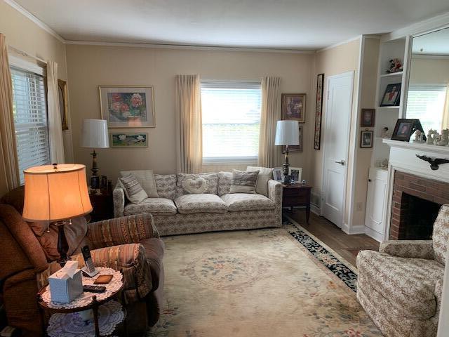 living room with crown molding, plenty of natural light, wood-type flooring, and a brick fireplace