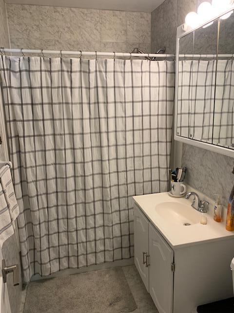 bathroom featuring walk in shower, vanity, and tile walls