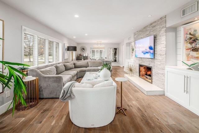 living room featuring built in shelves, a stone fireplace, a notable chandelier, and light hardwood / wood-style flooring