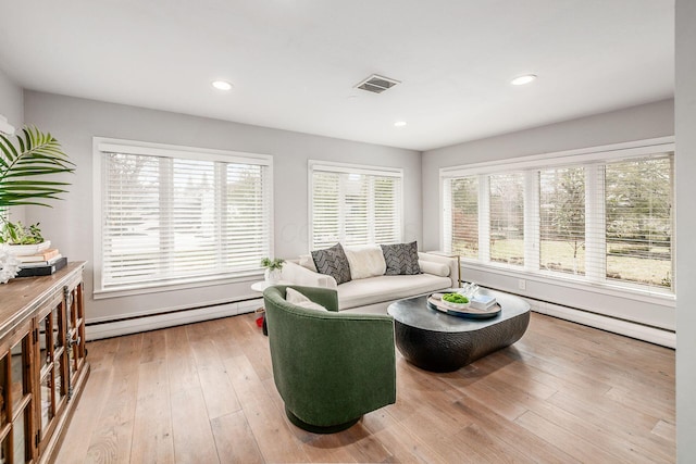 living room with a baseboard heating unit, a wealth of natural light, and light hardwood / wood-style floors