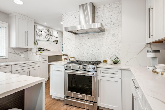 kitchen with wall chimney range hood, white cabinetry, stainless steel range with gas stovetop, light stone counters, and light hardwood / wood-style floors