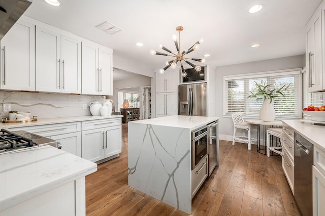 kitchen with light hardwood / wood-style flooring, appliances with stainless steel finishes, a center island, light stone counters, and white cabinets