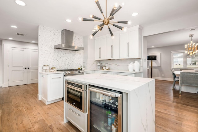 kitchen featuring white cabinets, beverage cooler, a center island, an inviting chandelier, and wall chimney exhaust hood