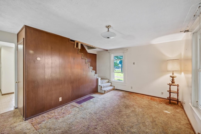 unfurnished bedroom featuring a textured ceiling, light colored carpet, and wood walls