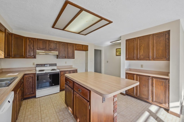 kitchen with a textured ceiling, a center island, white appliances, and sink