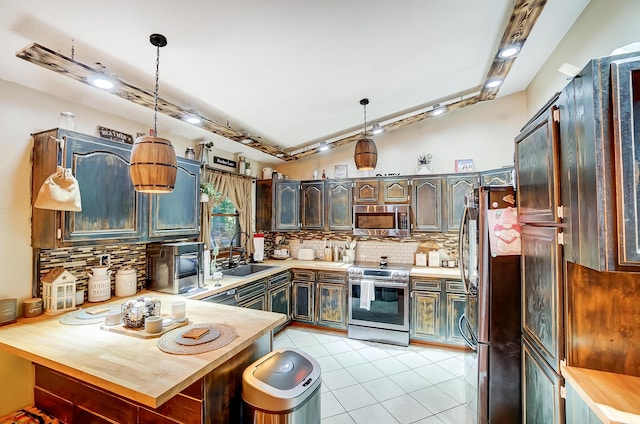 kitchen featuring kitchen peninsula, appliances with stainless steel finishes, backsplash, sink, and pendant lighting