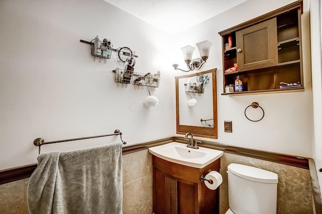 bathroom featuring vanity, a textured ceiling, toilet, and tile walls