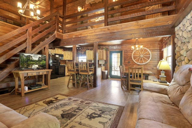 living room featuring beam ceiling, a high ceiling, a chandelier, wood-type flooring, and wooden walls