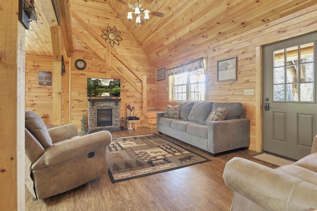 living room featuring ceiling fan, wood walls, a stone fireplace, and wood-type flooring