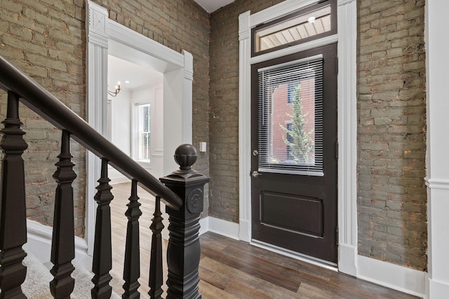 foyer featuring dark hardwood / wood-style flooring, a chandelier, and brick wall