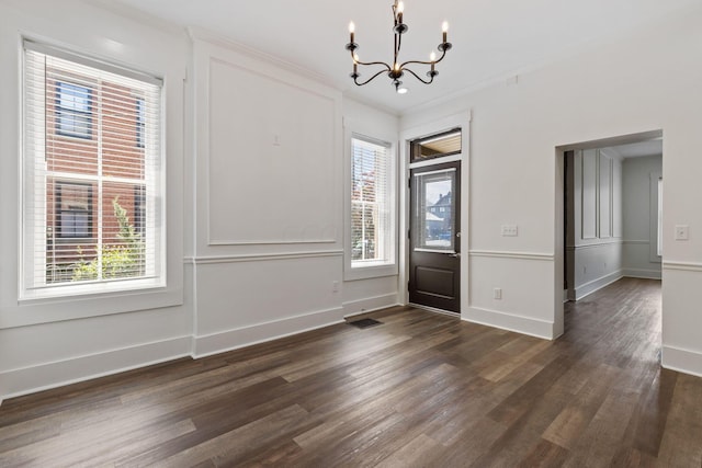 interior space featuring plenty of natural light, ornamental molding, dark wood-type flooring, and an inviting chandelier