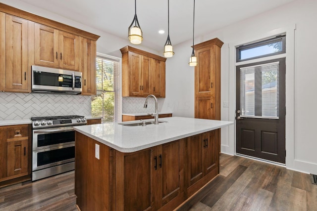 kitchen featuring pendant lighting, sink, an island with sink, appliances with stainless steel finishes, and dark hardwood / wood-style flooring