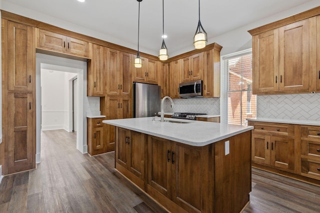 kitchen featuring sink, an island with sink, decorative light fixtures, dark hardwood / wood-style flooring, and stainless steel appliances