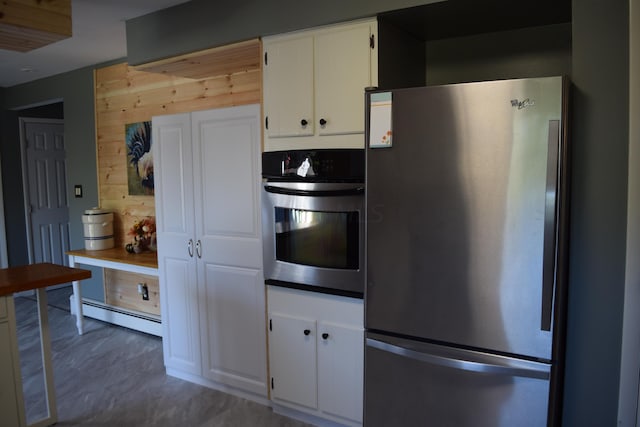 kitchen featuring white cabinets, appliances with stainless steel finishes, baseboard heating, and wooden walls