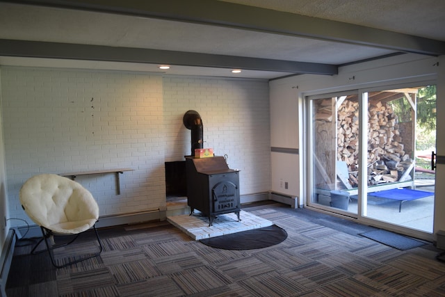 living area featuring beam ceiling, a wood stove, dark colored carpet, baseboard heating, and brick wall