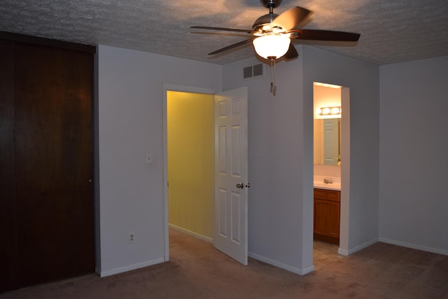 unfurnished bedroom with ceiling fan, light colored carpet, ensuite bathroom, and a textured ceiling